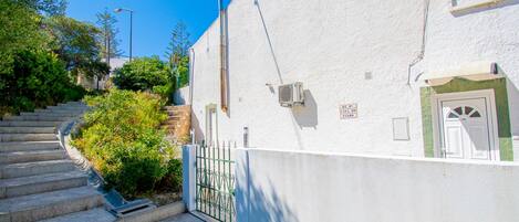 Un bâtiment blanc avec un escalier menant à l’étage, une porte en métal et une petite porte d’entrée.