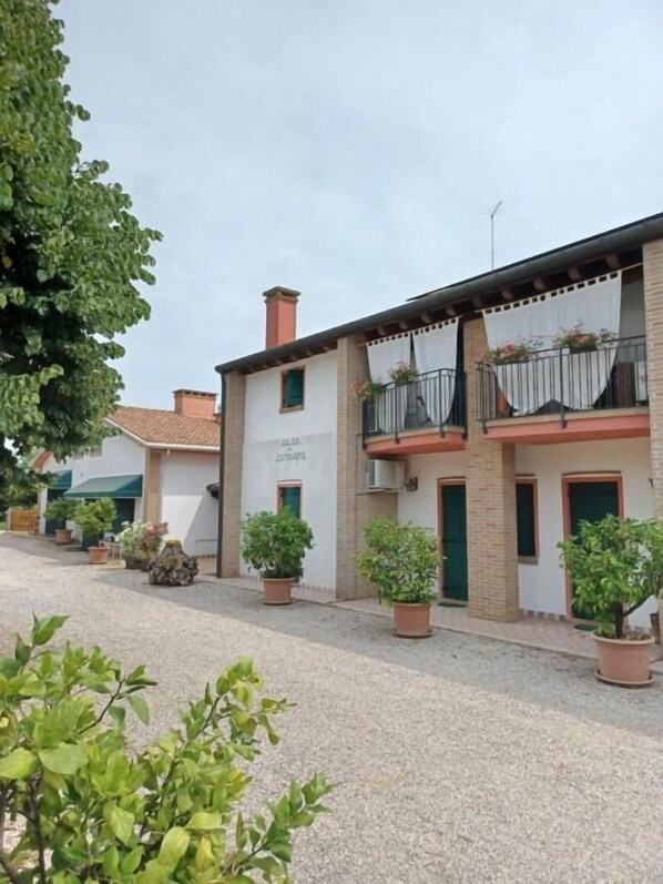 A building with a courtyard, potted plants, and a sign. - ALLOGGIO AGRITURISTICO ZAMBON (Vedelago)