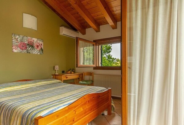 A bedroom with a bed, a desk, a chair, a window with a view, and an air conditioning unit. - ALLOGGIO AGRITURISTICO ZAMBON (Vedelago)