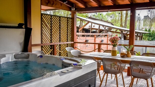 A hot tub on a wooden deck with chairs and a table, surrounded by a wooden fence and greenery. - Świdrowa Chata Jacuzzi & Sauna (Zakopane)