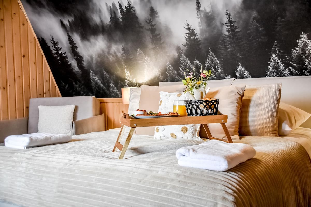 A bedroom with a bed, a tray with breakfast, a forest mural, and a wooden headboard.