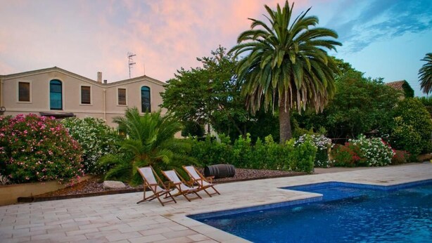 A swimming pool with lounge chairs, a palm tree, and a building with a tiled roof. - Mas Palou (El Pla del Penedès)