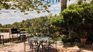 A patio with a round table and chairs, surrounded by potted plants and a stone wall. - Mas Palou (El Pla del Penedès)