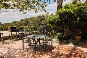 A patio with a round table and chairs, surrounded by potted plants and a stone wall.