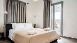 Una habitación de hotel con cama, cortinas, mesita de noche, lámpara y vistas a través de un ventanal.