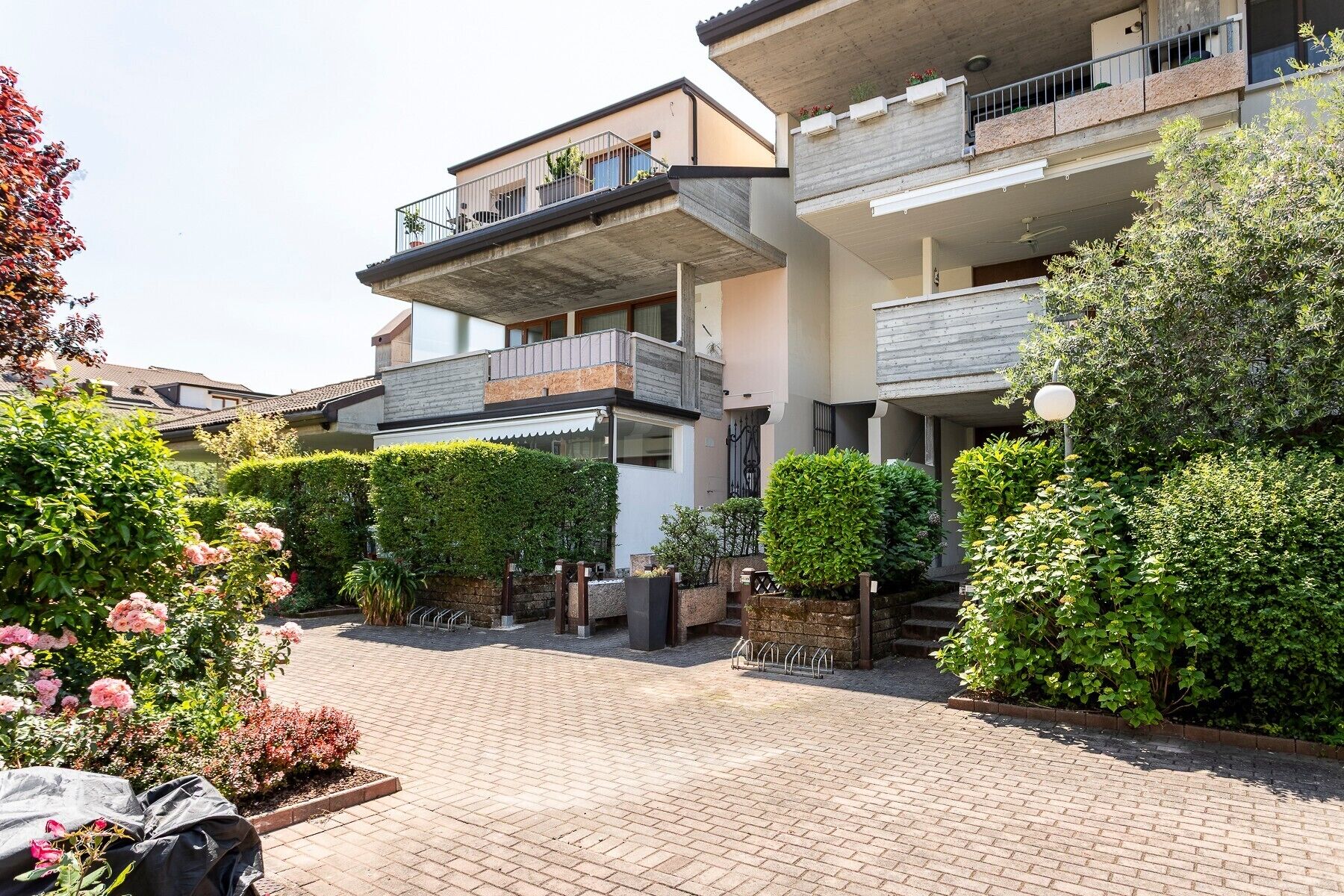 Un immeuble résidentiel à plusieurs étages, doté de balcons, d’une cour pavée et agrémenté de divers arbustes et plantes.