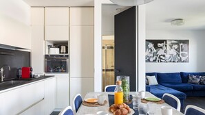 Una cocina moderna con comedor, una sala de estar con un sofá azul y un cuadro de Picasso en la pared.