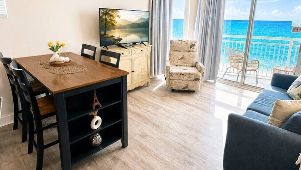 Een woonkamer met een eettafel, stoelen, een televisie, een bank en uitzicht op de oceaan.