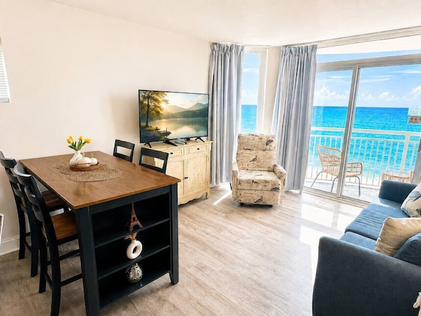 A living room with a dining table, chairs, a TV, a sofa, and a view of the ocean. - BEACH DAZE GETAWAY/PRIME LOCATION (Myrtle Beach)