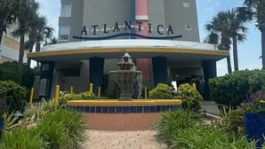 Een hoog hotelgebouw met de naam 'ATLANTICA' op de gevel, een fontein in het midden en omliggend groen.