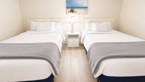 Een kamer met twee bedden, een nachtkastje met lamp en een afbeelding met strandthema aan de muur.