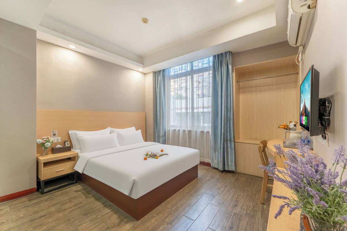 A hotel room with a bed, bedside table, TV, and a desk with a chair.