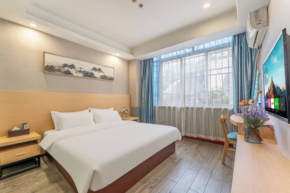 A hotel room with a large bed, a desk with a chair, a TV, and a window with curtains.