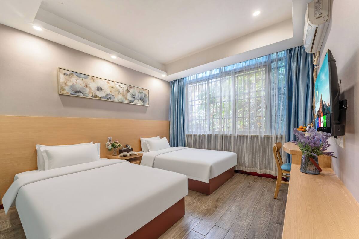 A hotel room with two beds, a desk, a chair, a TV, and a window with curtains.