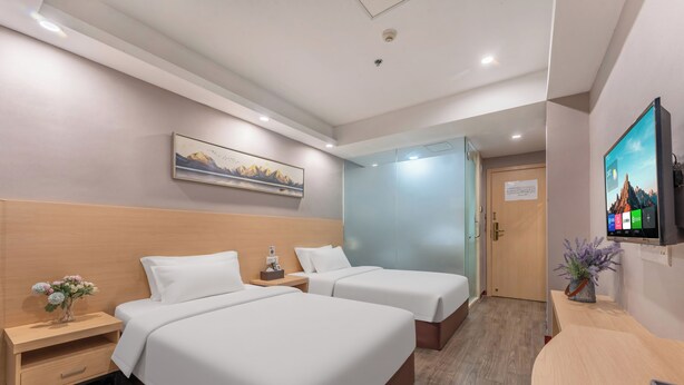 Ein Hotelzimmer mit zwei Betten, einem Schreibtisch, einem Fernseher, einem Gemälde und einer Tür zu einem anderen Raum.