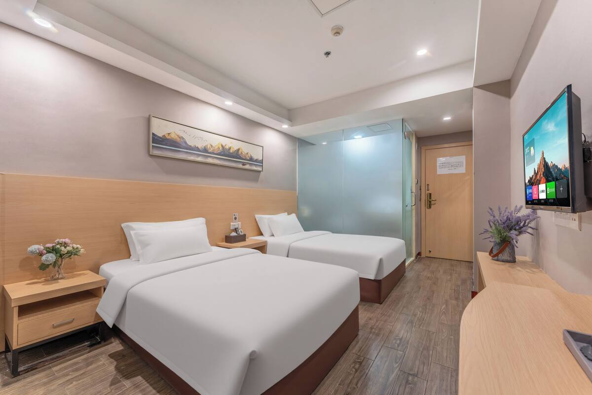 A hotel room with two beds, a desk, a TV, a painting, and a door leading to another room.