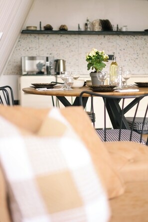 A dining area with a round table set for two, a potted plant, and a bottle of wine.