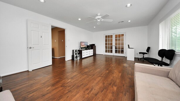 A spacious room with hardwood flooring, a ceiling fan, a TV, a sofa, and a door leading to another room. - Lofty Grace Home 2 (Richmond)