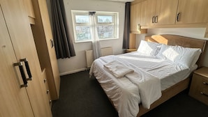 Ein Schlafzimmer mit Bett, Holzschrank, einem Fenster mit Vorhängen, einem Heizkörper und einem Nachttisch.