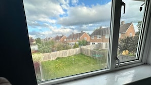 Ein Fenster mit Blick auf eine Wohngegend, einen Holzzaun und eine Rasenfläche.