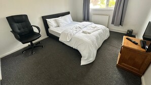 Ein Hotelzimmer mit Bett, Sessel, Schreibtisch, Fenster mit Vorhängen und Heizkörper.