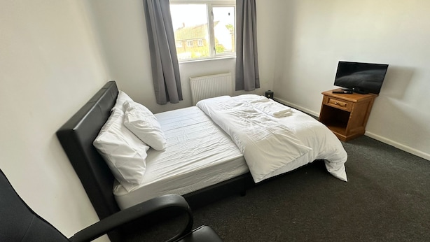 Ein Hotelzimmer mit einem Bett, einem Fernseher auf einem Nachttisch aus Holz und einem Fenster mit Vorhängen.
