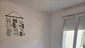 A bedroom with a bed, a window, and a wall-mounted decoration. - Apartment 10 minutes walk from the beach first floor with terrace (Clairvaux-les-Lacs)