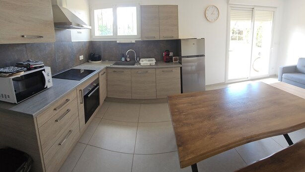 A modern kitchen with a wooden table, built-in appliances, and a view to the outside. - Apartment 10 minutes walk from the beach first floor with terrace (Clairvaux-les-Lacs)