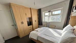 Ett sovrum med en säng, en garderob, en tv och ett fönster med gardiner.