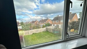 Ett fönster med utsikt över ett bostadsområde, ett trästaket och en gräsklädd trädgård.