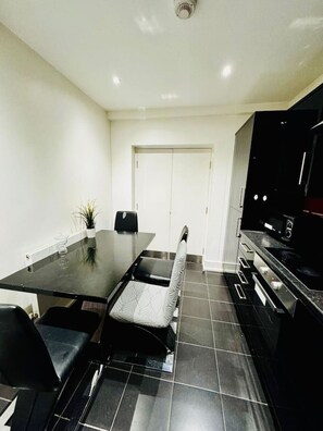 A modern kitchen with a dining table, chairs, a black countertop, and a black TV. - Big one bedroom flat with separate kitchen (Greater London)