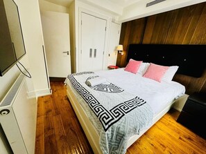 A bedroom with a bed, a nightstand, a wall-mounted TV, a wooden floor, and a white door. - Big one bedroom flat with separate kitchen (Greater London)