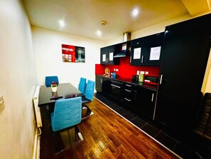 A compact kitchen with black cabinets, a red backsplash, and a dining area with a wooden table and blue chairs. - Beautiful one bedroom flat in London (Greater London)