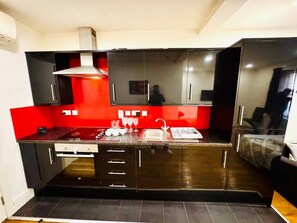 A compact kitchen with dark cabinetry, a red backsplash, and a stainless steel range hood. - Beautiful one bedroom flat in London (Greater London)