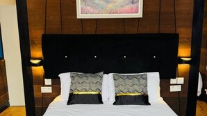 Una cama doble con cabecera de madera, dos lámparas de noche y un cuadro en la pared superior.