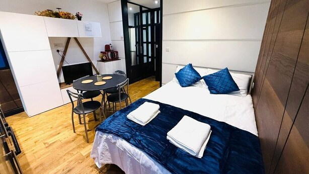 Una habitación de hotel compacta con una cama, una pequeña mesa con sillas y una zona de kitchenette.