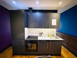 A compact kitchen with dark cabinetry, a built-in oven, a sink, and a kettle. - Amazing one bedroom flat in London city (Greater London)