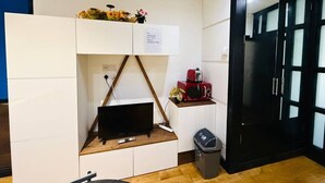 Habitación compacta con televisión integrada, un pequeño estante con microondas y un cubo de basura.