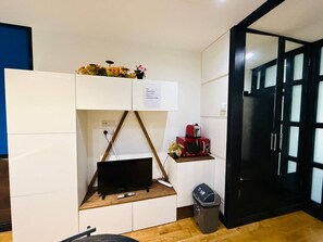 A compact room with a built-in TV, a small shelf with a microwave, and a trash bin. - Amazing one bedroom flat in London city (Greater London)