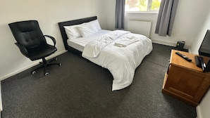 Ein Hotelzimmer mit Bett, Sessel, Schreibtisch, Fenster mit Vorhängen und Heizkörper.