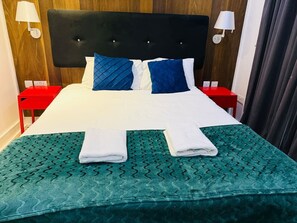 A neatly made bed with a green patterned bedspread, two pillows, and two folded towels. - Specious one bedroom flat in Whitechapel (Greater London)