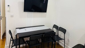 A room with a flat-screen TV mounted on the wall, a rectangular table with a white tablecloth, and six black chairs. - Specious one bedroom flat in Whitechapel (Greater London)