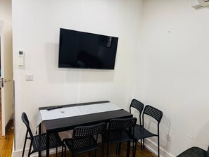 A room with a flat-screen TV mounted on the wall, a rectangular table with a white tablecloth, and six black chairs. - Specious one bedroom flat in Whitechapel (Greater London)