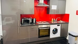 A compact kitchen with stainless steel appliances, a washing machine, and a red accent wall. - Specious one bedroom flat in Whitechapel (Greater London)