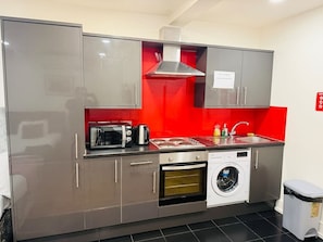 A compact kitchen with stainless steel appliances, a washing machine, and a red accent wall. - Specious one bedroom flat in Whitechapel (Greater London)
