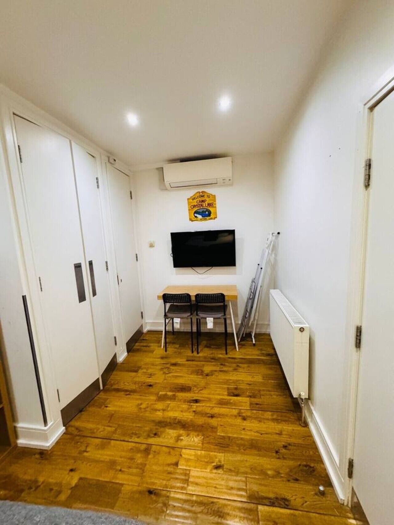 Un couloir avec un plancher en bois, des murs blancs, un téléviseur fixé au mur et une enseigne au-dessus.