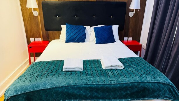 A neatly made bed with a teal bedspread, two pillows, and two folded towels. - Specious one bedroom flat in Whitechapel (Greater London)