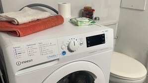 En tvättmaskin med frontmatning, ett kontrollpanel, en vit toalett och en handduk ovanpå.