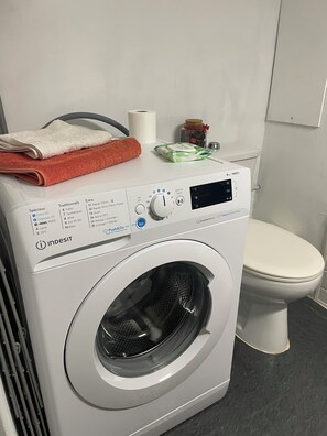 A front-loading washing machine with a control panel, a white toilet, and a towel on top. - Swiss border 10 minutes from downtown Geneva 50m from tramway (Gaillard)