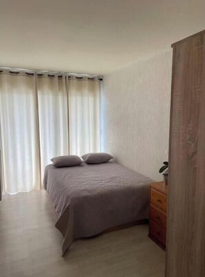 A bedroom with a bed, curtains, a wooden dresser, and a plant. - Swiss border 10 minutes from downtown Geneva 50m from tramway (Gaillard)
